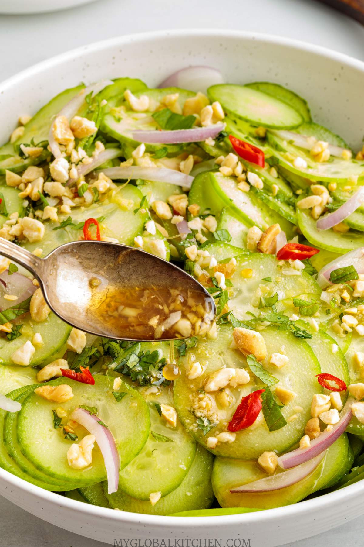 Close up of cucumber salad in a bowl with a spoon adding a dressing to it