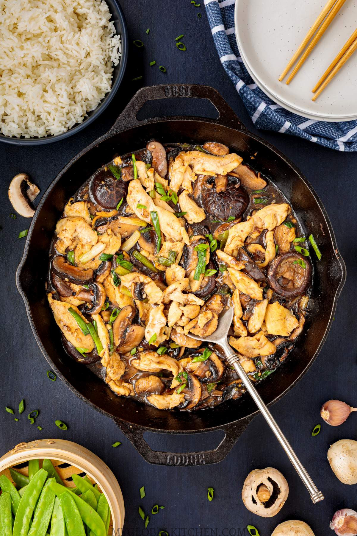 Overhead view of a skillet filled with Chinese Chicken and Mushroom stir fry, next to a bowl of rice and veggies