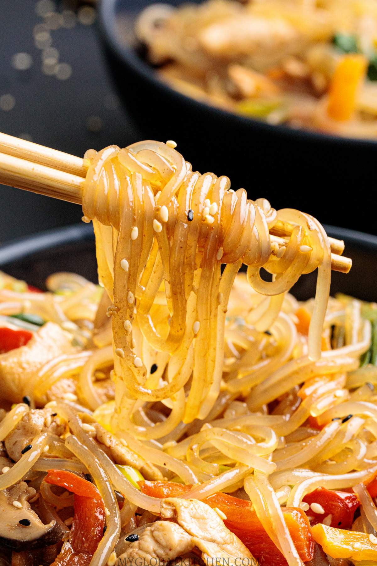 Two chopsticks showing the Korean glass noodles from a bowl of  Japchae