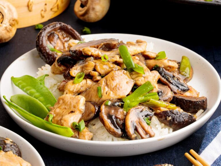 A plate of Chinese Chicken and Mushroom Stir Fry or Moo Goo Gai Pan on top of rice in a white bowl