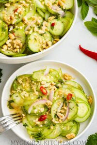 Two bowls full of Thai Cucumber Salad,, with some chilies and fresh herbs