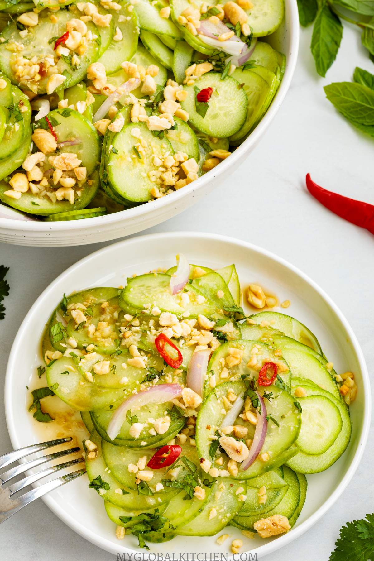 Two bowls full of Thai Cucumber Salad,, with some chilies and fresh herbs