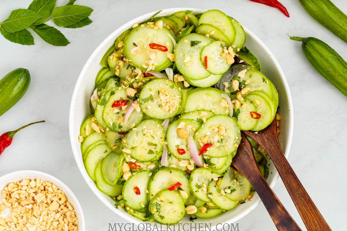 Overhead view of a white bowl full of cucumber salad with two serving spoons