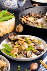 Side view of a plate of Chinese Chicken and Mushroom Stir Fry or Moo Goo Gai Pan on top of rice in a white bowl