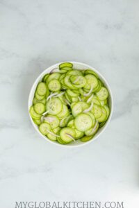 Sliced cucumbers and red onion slices in a white bowl