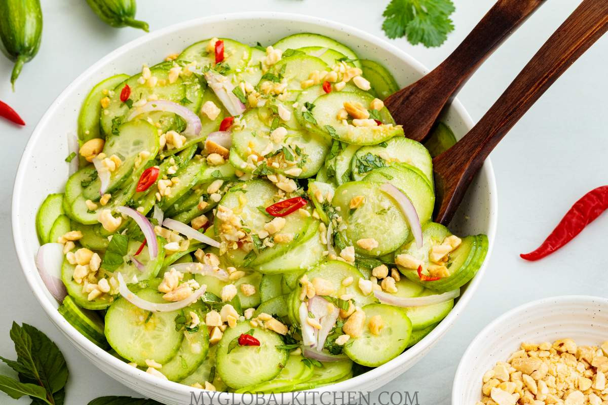 Thai Cucumber salad with crushed peanuts, onions and red chilies in a white bowl with two serving spoons