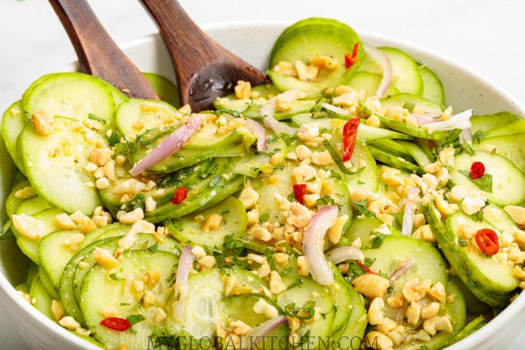 Close up of a cucumber salad being tossed in a white bowl